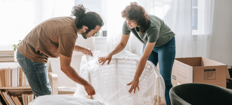 two people wrapping a chair representing how to pack your household for a move from Brooklyn to New Jersey