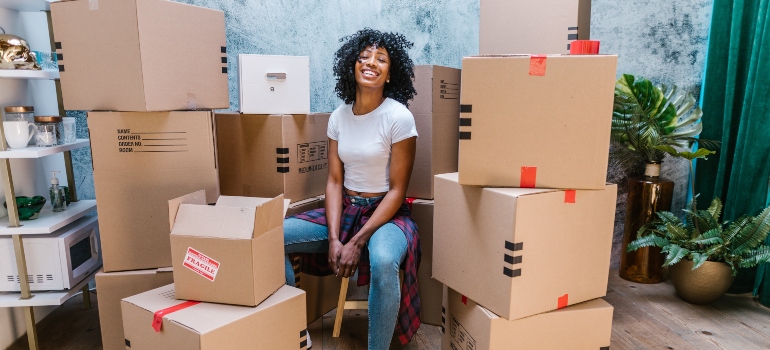 happy young black woman with moving boxes behind her representing moving out of your parents home for the first time