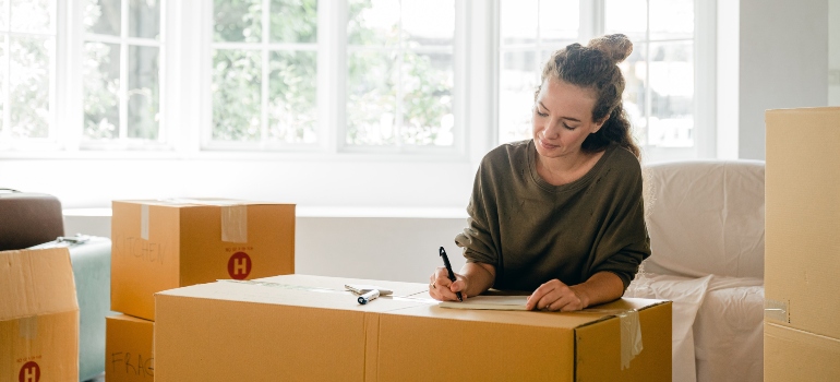A woman moving out writing on a cardboard box.