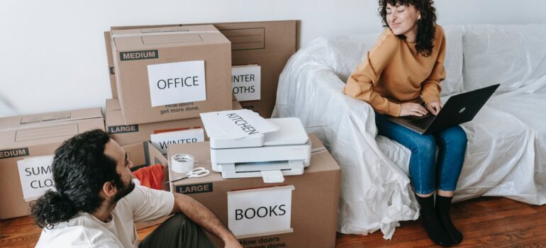 A couple sitting besides packed and labeled boxes and the woman is looking at what to pack first and what last when moving long-distance from Manhattan