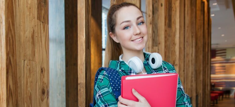 Girl with the book in her arms and headphones around her neck in the hallway 