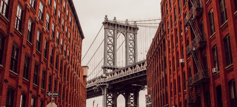 The Brooklyn bridge seen between two red buildings in one of the best neighborhoods to buy a condo in NYC