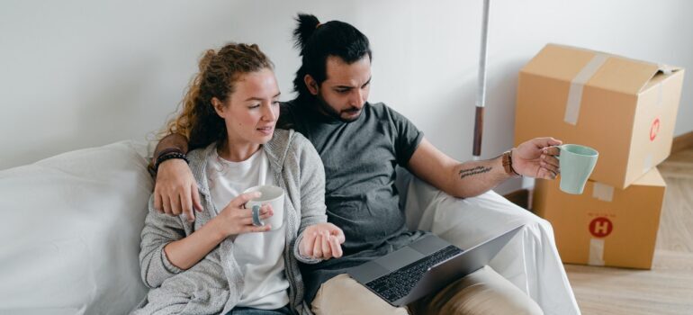 Couple surrounded by moving boxes looking at the laptop following the tips on how to do your research if you want to make your long distance house hunt a success