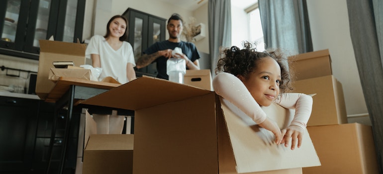 Family getting ready for a relocation and a girl sitting inside a cardboard box waiting for Forest Hills movers to arrive